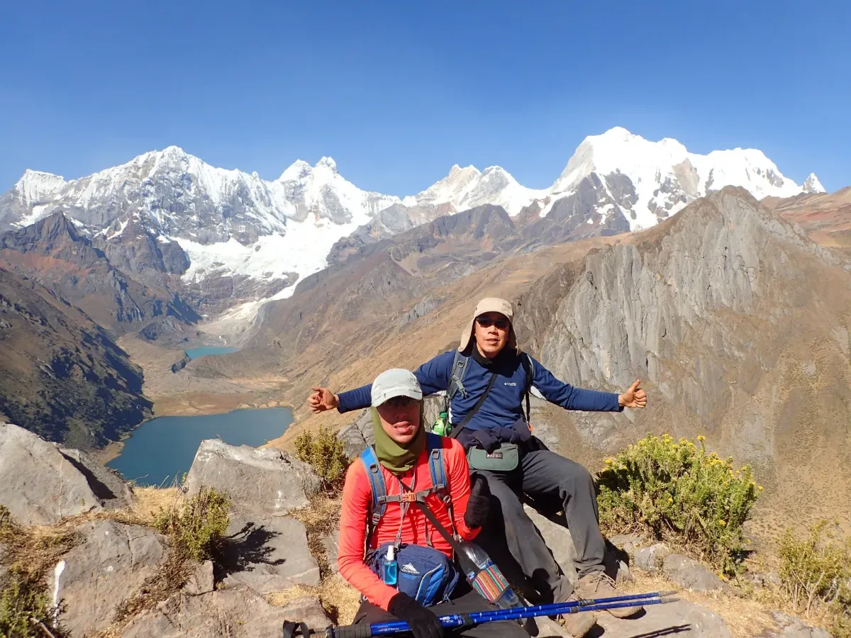 Two happy trekkers above a lake with snow peaks behind