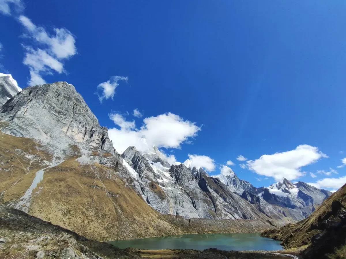 A lake beneath grey limestone cliffs and snow peaks
