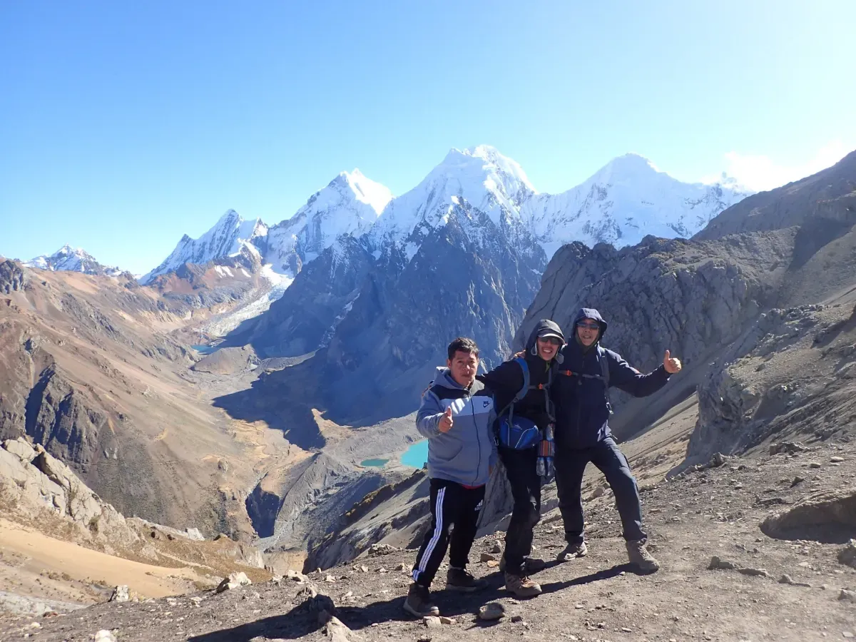 Three trekkers posing in front of a snow-capped massif