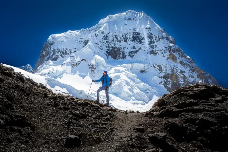 A trekker standing before a huge snow-covered mountain face